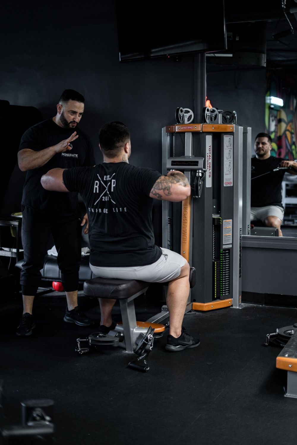 Roger Rojas coaching a client's form on a cable machine at Incinerate